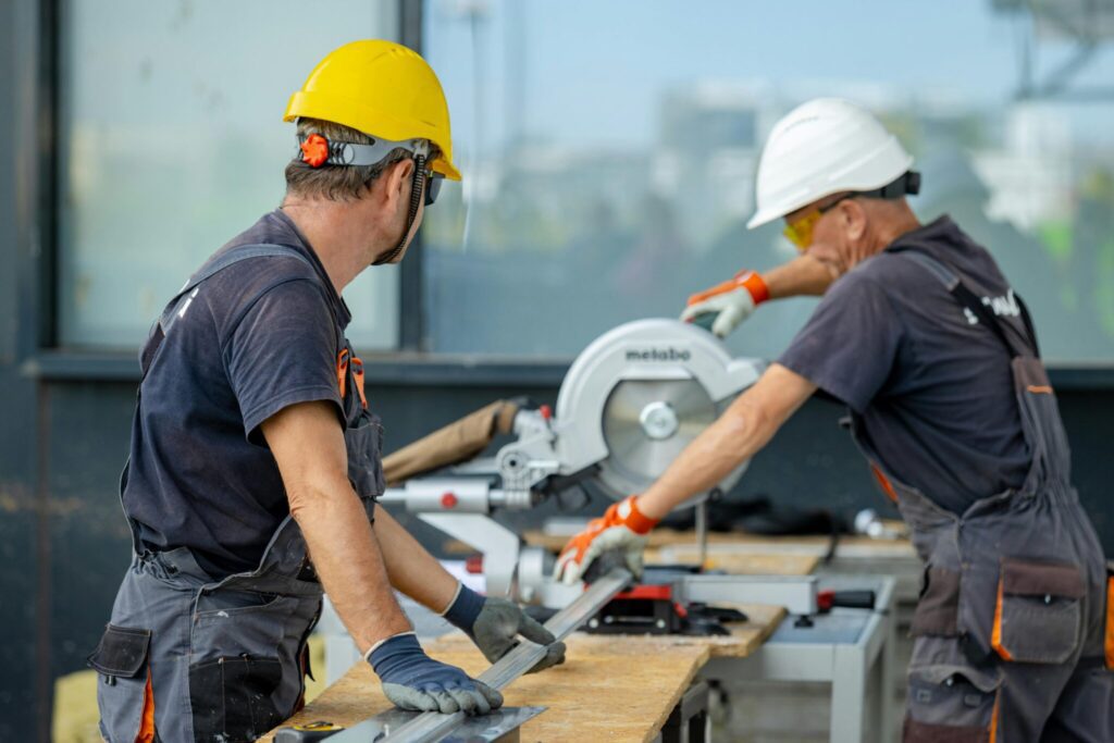Two construction workers cutting metal using a bench saw
