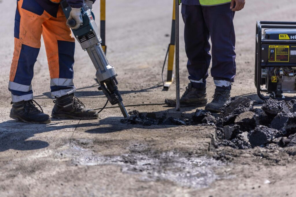 Road workers breaking concrete using a jackhammer.