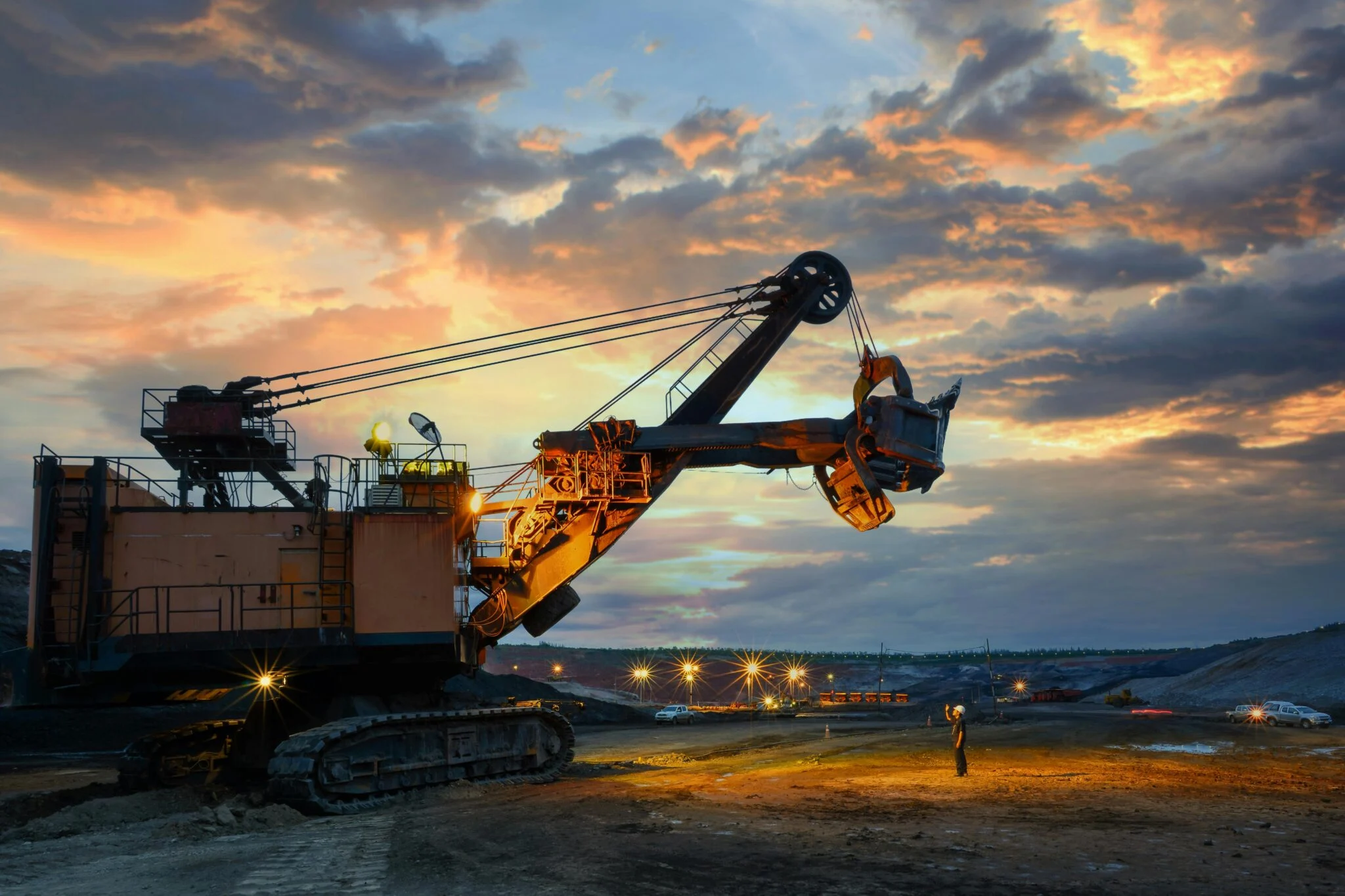 Giant mining dragline at sunset with a worker below.