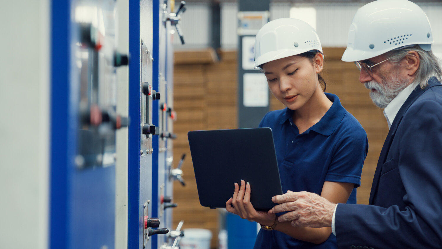 Two mine site workers reviewing data on a laptop next to an electrical control panel