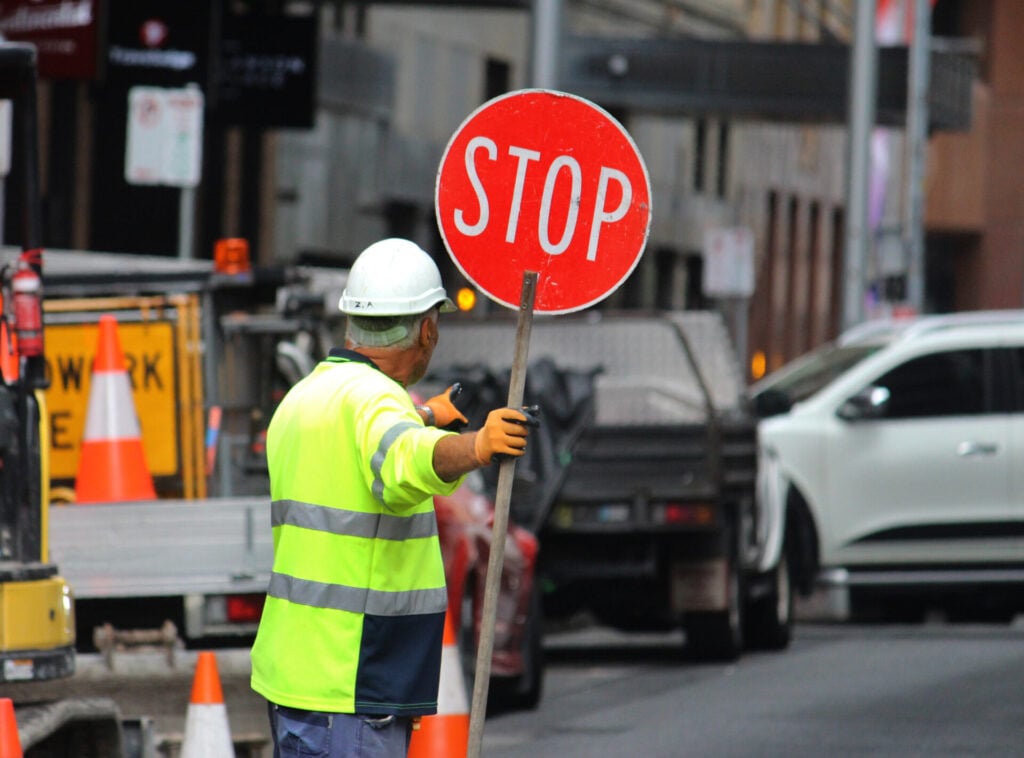 Traffic controller holding stop sign on busy city street during roadworks