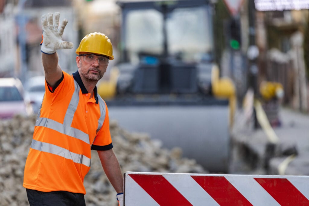 Traffic controller in hi-vis vest and hard hat directing traffic at road construction site